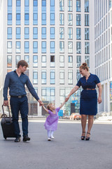 Family with a suitcase in the background of a tall building. The family is moving.