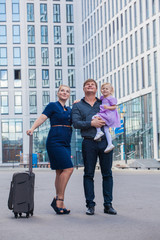 Fototapeta premium Family with a suitcase in the background of a tall building. The family is moving.