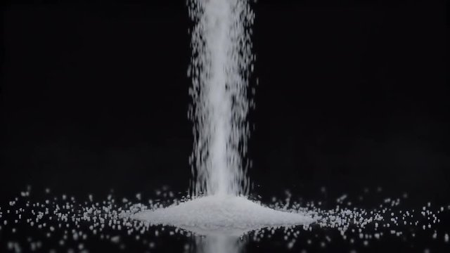 Pouring white sugar on black background in slow motion.