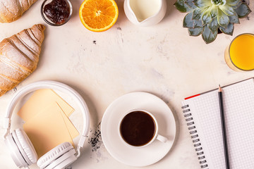 Notepad, headphones, croissants and coffee on white table.