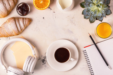 Notepad, headphones, croissants and coffee on white table.