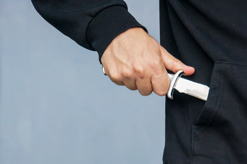 Hand from the pocket of the black jacket pulls out a folding knife close up.