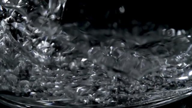 Closeup of fresh mineral water falling in glass on black background. Pure and fresh energy in water for a healthy life. Slow motion shot.
