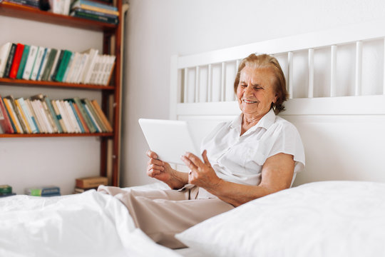 Elderly woman sitting comfortably on bed and using her tablet