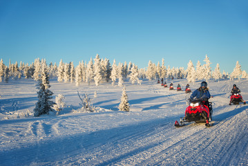 Group of tourists riding snowmobiles in a snowy winter landscape in Lapland, near Saariselka,...