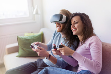 Happy young couple playing video games with virtual reality headsets