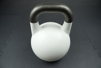 Naklejka na ściany i meble White 10kg competition kettlebell on a fitness studio gym floor with rubber tiles. Potential text space at center of kettlebell.