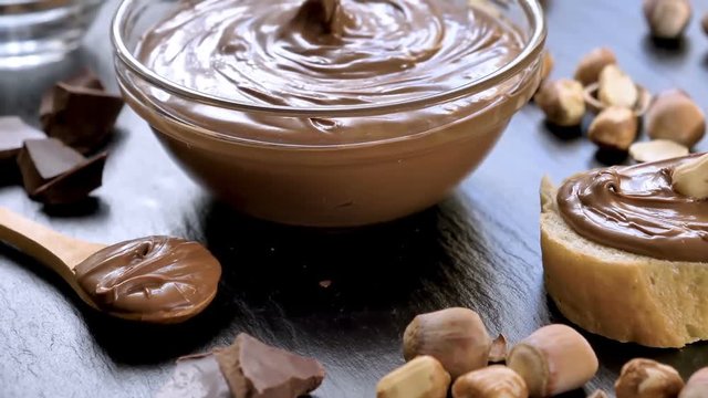 Chocolate spread in glass bowl with hazelnuts on black table. Serving a delicious breakfast concept. Dolly shot.