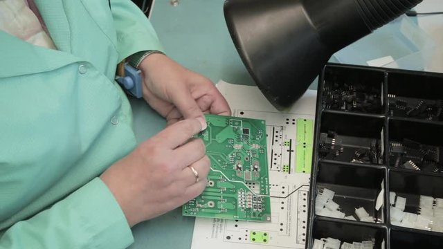 Woman holding pincette and soldering iron instal electronic components on PCB (Printed circuit boards)