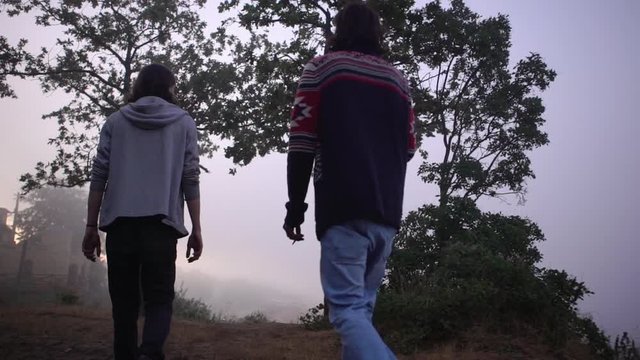 footage from back early in morning two tall slim men walking to the edge of hill to play footbag freestyle over coastal city covered with fog in slow motion