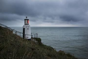 Fototapeta na wymiar Lighthouse shining its red beacon on a gloomy day , Polperro, Cornwall, UK