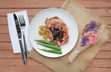 Pork steak with vegetables and knife - fork on a white plate against wood plank background.