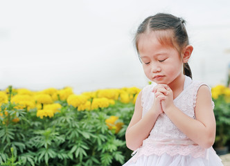 Adorable little asian girl praying at the garden. Spirituality and religion.