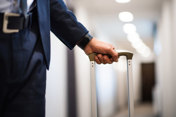 Unrecognizable businessman with luggage in a hotel corridor.