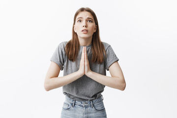 I promise. Portrait of handsome young caucasian brunette girl with dark eyes in casual t-shirt and jeans holding palms together in pleasing gesture, asking for one more chance from teacher.