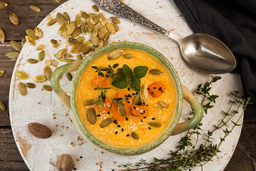 Pumpkin soup in beige bowl with pieces of pumpkin, seeds and herbs on old wooden background.