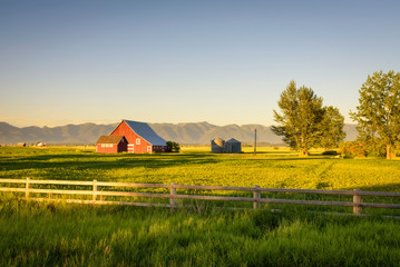 Summer sunset with a red barn in rural Montana and Rocky Mountains - obrazy, fototapety, plakaty