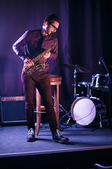Male saxophone player on a stage. Drums on a background