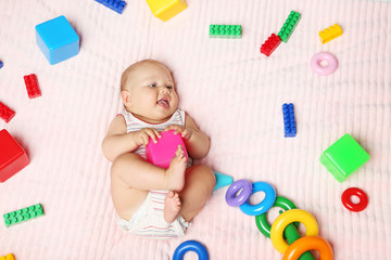 Little newborn baby with toys on pink bed