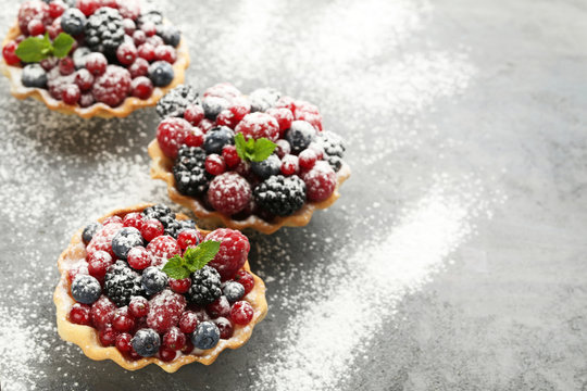 Tasty tartlet with berries and powdered sugar on grey wooden table