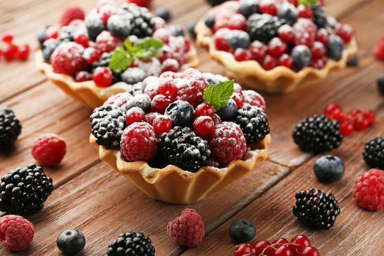 Tasty tartlet with berries and powdered sugar on brown wooden table