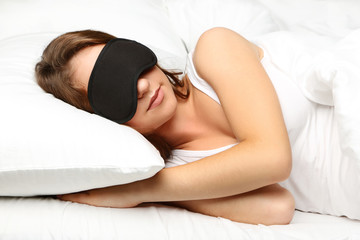 Young woman sleeping with eyemask in white bed