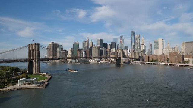 A daytime wide panoramic establishing shot of the Manhattan Skyline with a barge traveling under the Brooklyn Bridge.  