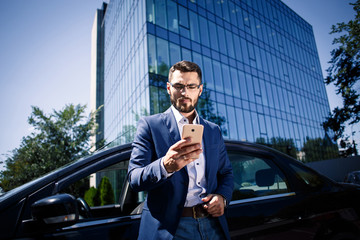 Young businessman standing near the car and holding phone