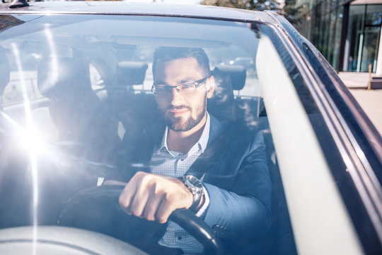 Portrait of smiling young business man wearing a jacket and driving a business class car
