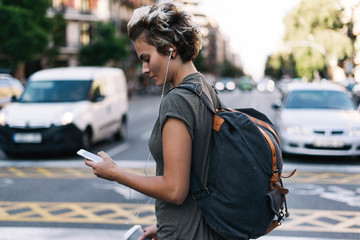 Young blonde woman is walking the city streets with the travel apps on her mobile phone. Hipster...