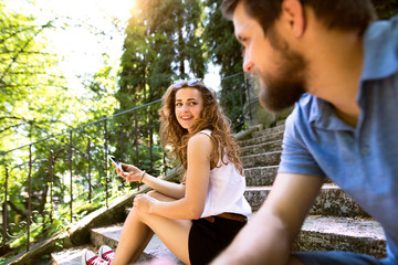 Fototapeta premium Young couple with smartphone sitting on stairs in town.