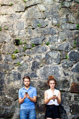 Obraz na płótnie Canvas Young couple with smartphones against stone wall in town.