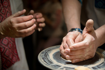 Obraz na płótnie Canvas Teacher man teaches a child how to make a ceramic plate on the potter's pile. Close-up of child's hands and masters.