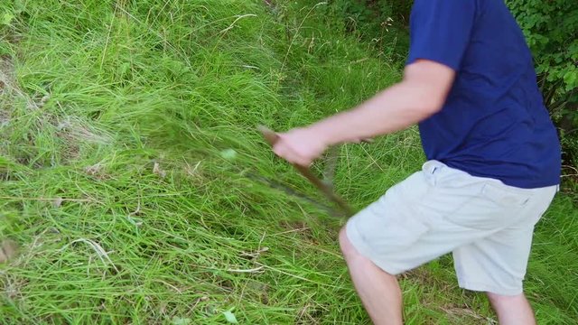 Man mowing grass with a scythe by hands. Mowing on hill slope where motor machine mower cant do the job. Filmed in slow-motion hd.