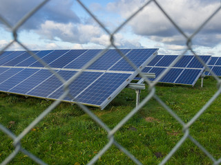 Solar panel or photovoltaic farm behind metal chainlink fence on green field with dramatic cloudy...
