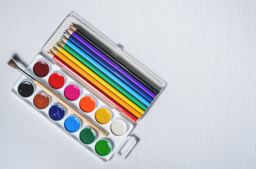 Bright colored watercolor paints and pencils, top view, white background.