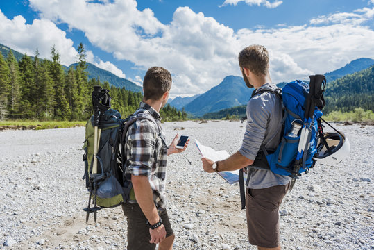 Germany, Bavaria, two hikers standing in dry creek bed orientating with cell phone and map