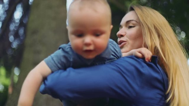 closeup adorable little baby boy mother hands holding green park looking camera interested look eyes happy emotions face portrait chubby cheeks throwing up funny playing sunny day smiling cheerful