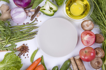 Fresh organic vegetables and seasoning ingredients for tasty vegetarian cooking around blank white plate , top view.