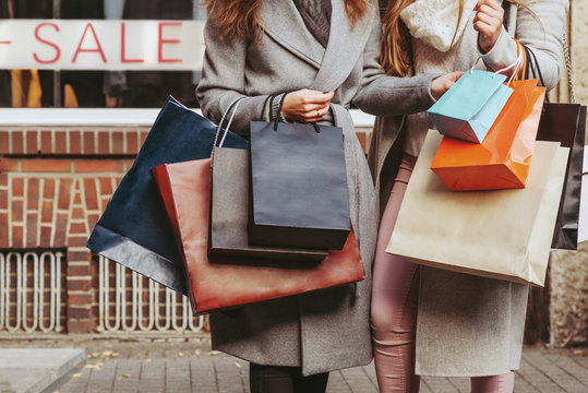 two girls with shopping bags in front of showwindow with sale writting on it