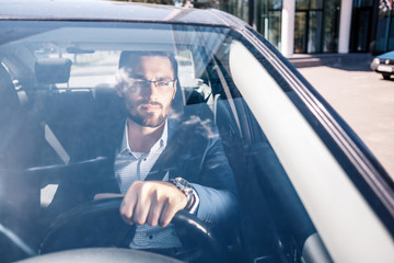 Serious looking man in glasses seating in black car