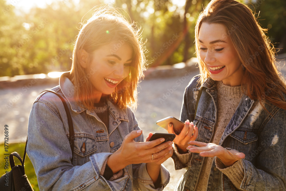 Sticker Two happy exited young woman friends looking at smartphones in park outdoor