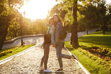 Fototapeta premium Two happy young brunette girls in jeans casual wear hug each other, holding hands while walking in the park outdoors
