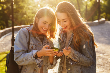 Two happy female best friends using smartphone in sunny park