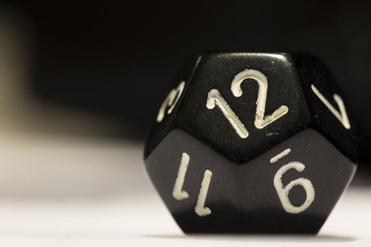 Macro shot of a black twelve-sided die on side showing a twelve