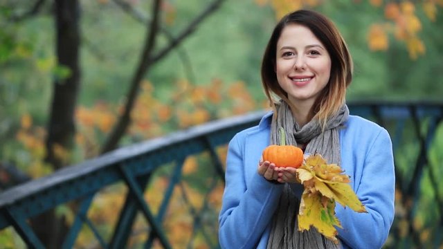 Young redhead girl with leaves and pumpking in park