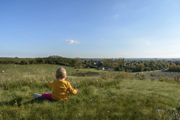 small child in bright clothes, sitting on a high hill opens a beautiful view