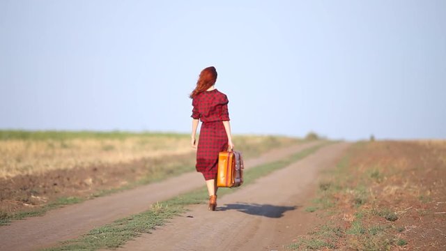Young redhead girl walking with travel suitcase at countryside road