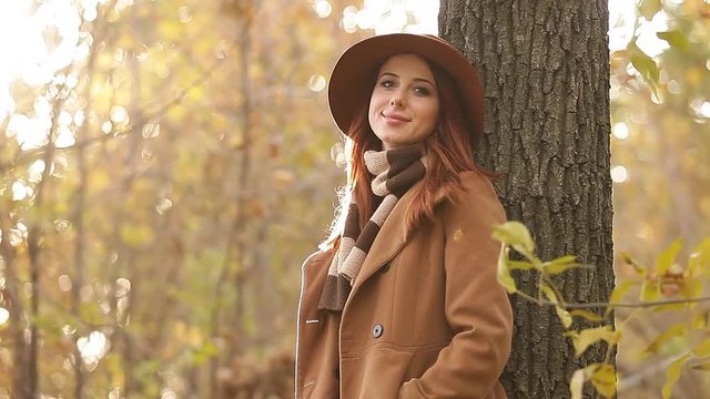 Redhead girl in yellow hat and coat with scarf on autumn park
