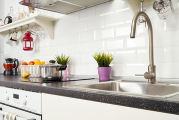 Interior of a light kitchen in the apartment. Bright home interior decoration items, fruit, flowers in a pot, steel hood. Bright ready-made picture for your individual design                     